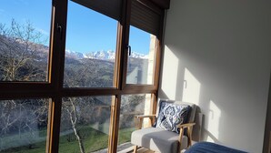 A bedroom with large windows, a bed, a chair, and a view of mountains. - Apartment with views to the Picos de Europa 4 pax - 1 (Tollo)