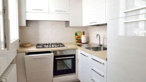 Una cocina compacta con armarios blancos, una estufa a gas, un lavavajillas y un refrigerador.