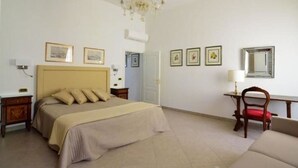 Un dormitorio con cama, escritorio, silla, candelabro y cuadros en la pared.