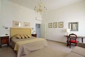 A bedroom with a bed, a desk, a chair, a chandelier, and framed pictures on the wall. - Sissi Suite (Venice)