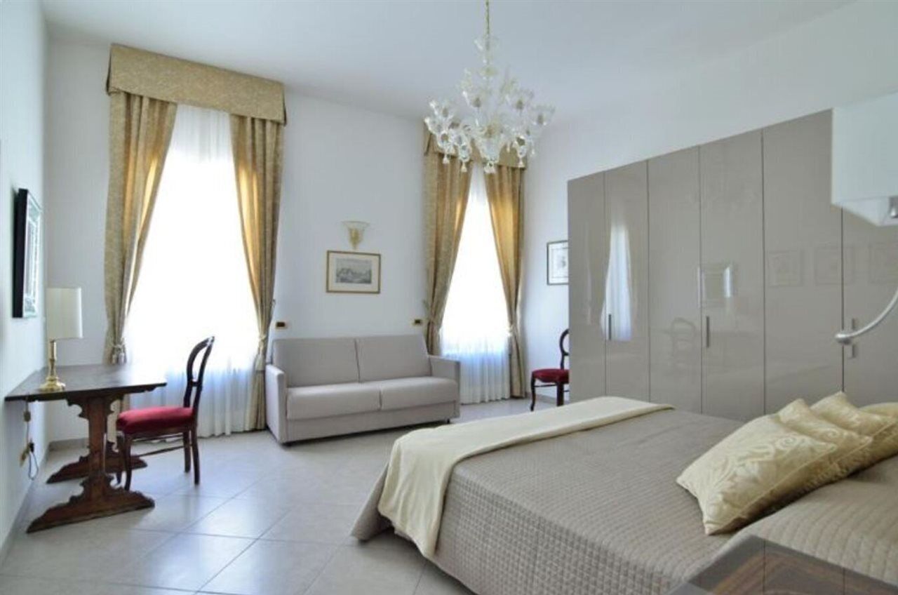 A hotel room with a bed, a sofa, a dining table, and a chandelier.