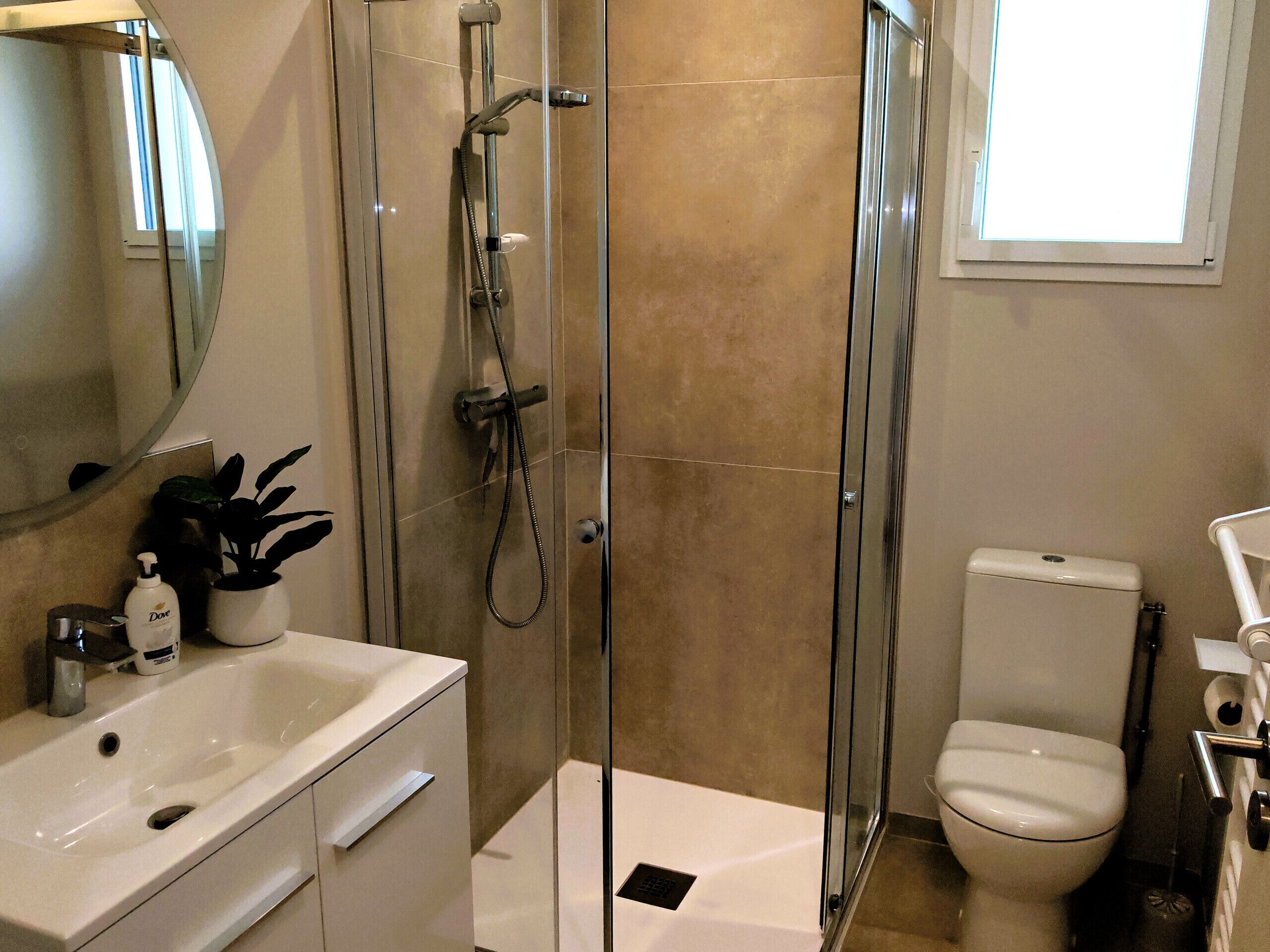 Un baño moderno con ducha de vidrio, lavamanos blanco, inodoro y espejo.