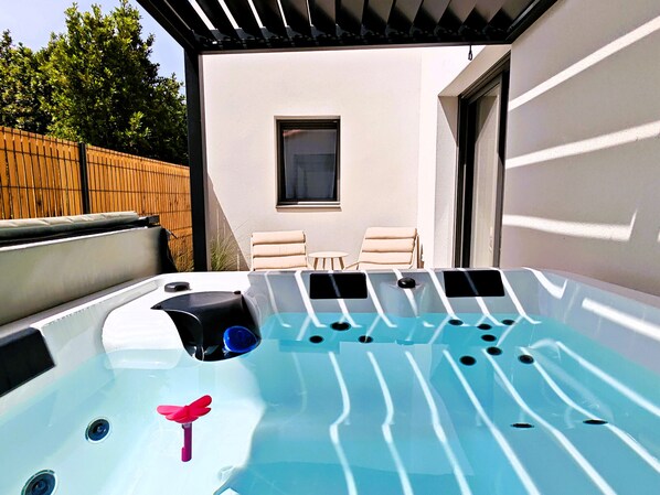 Ein Whirlpool mit Bedienfeld, zwei Liegestühle und ein Fenster in einem Garten.