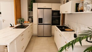 Una cucina moderna con mobili bianchi, un frigorifero a doppia anta, forno incassato e un piano di lavoro in marmo.