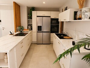 Eine moderne Küche mit weißen Schränken, einem Side-by-Side-Kühlschrank, einem Einbauofen und einer Marmorarbeitsplatte.