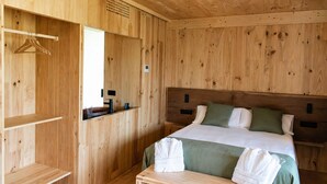 A wooden room with a bed, a hanging rack, and a small table.