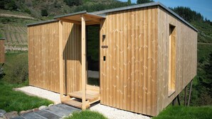 A wooden cabin with a door open, a small porch, and a gravel path leading to it.