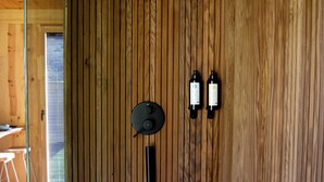 A wooden wall with a shower head, two bottles, and a hose.