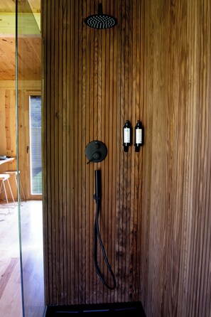 A wooden wall with a shower head, two bottles, and a hose.