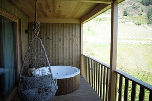 A wooden deck with a hot tub and a hanging chair overlooking a green landscape.