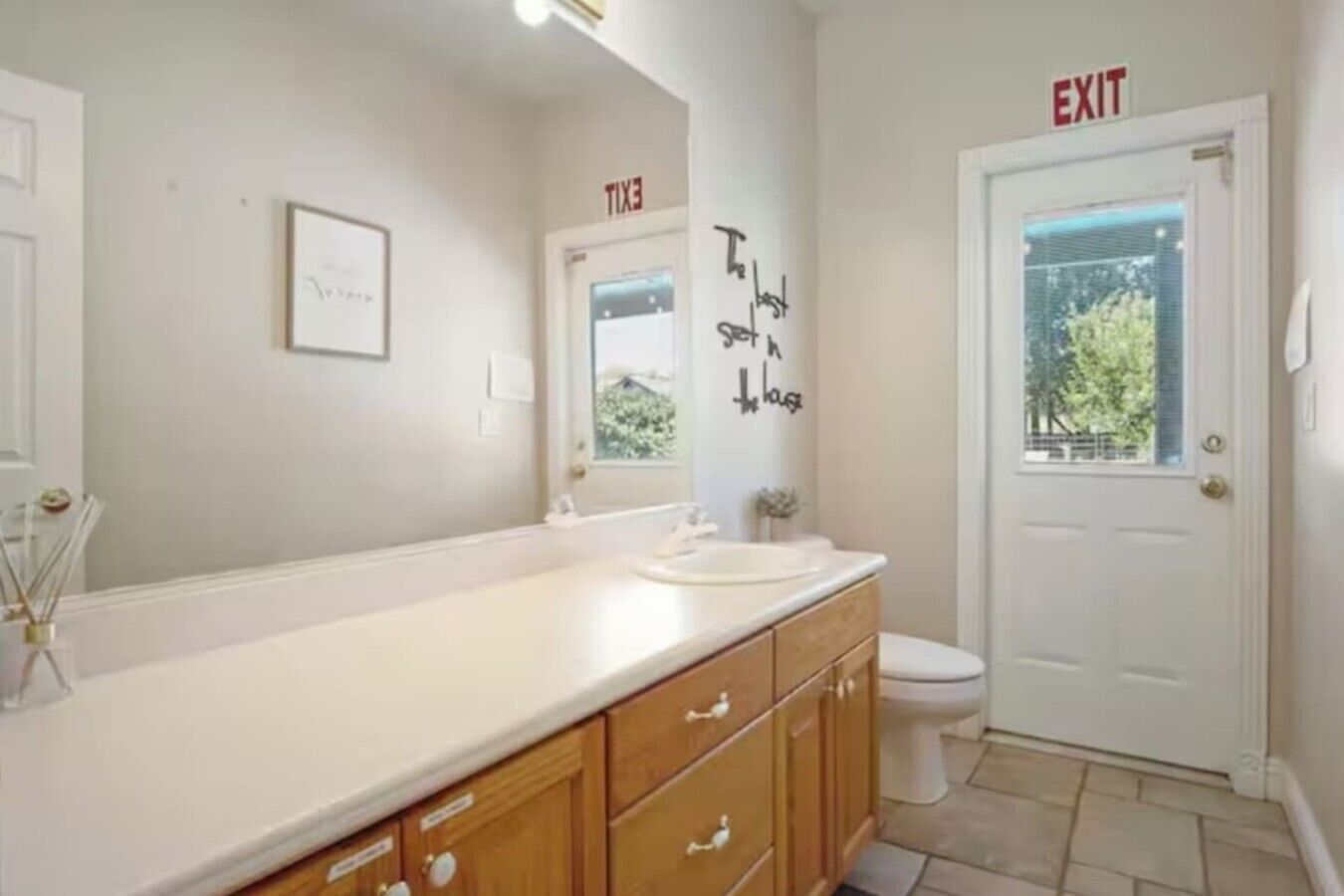 Une salle de bain avec un lavabo blanc, des meubles en bois, des toilettes et une porte de sortie.