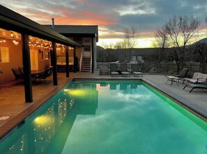 En swimmingpool med en täckt uteplats, utomhusmöbler och utsikt över solnedgången.