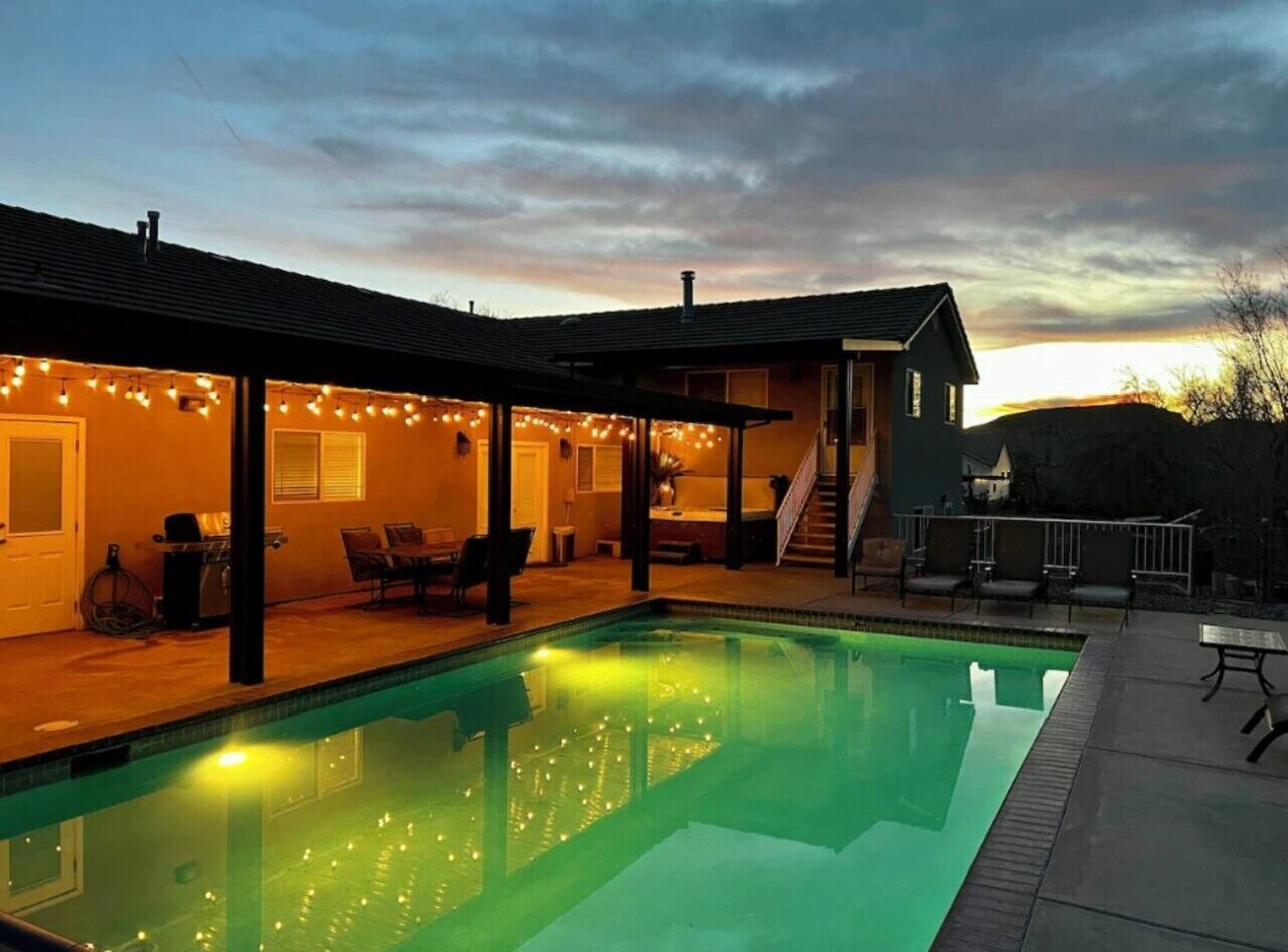 Une piscine avec éclairage, un patio couvert et une maison avec un escalier.