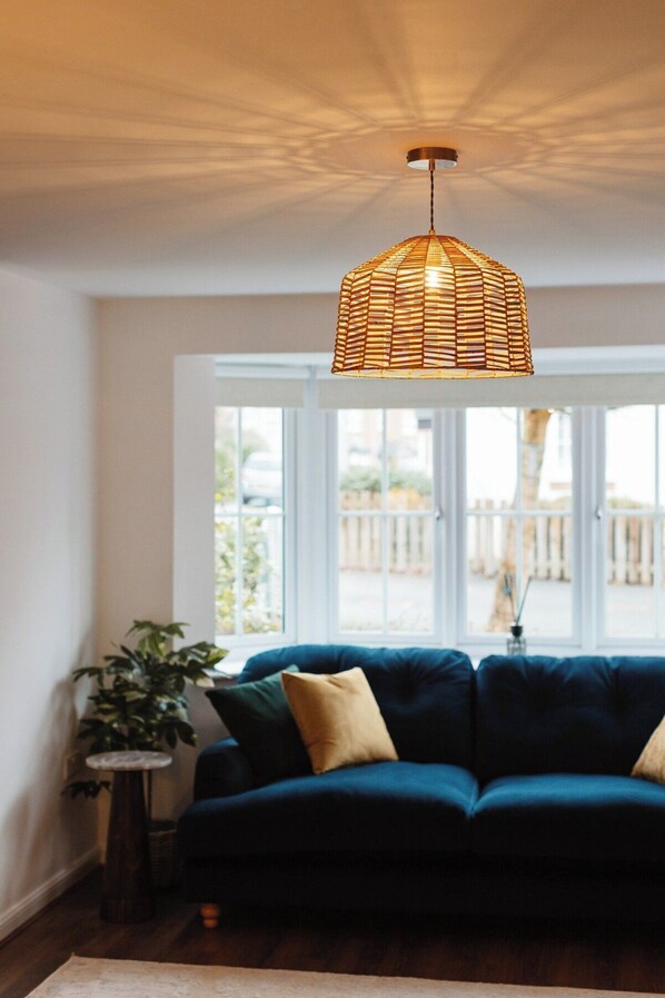 Een kamer met een donkerblauwe bank, een rotan hanglamp en een groot raam met uitzicht.