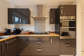 Een moderne keuken met donkere kastjes, een gasfornuis, een inbouwoven en een koffiezetapparaat.