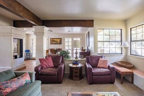Ein geräumiges Wohnzimmer mit zwei Ledersofas, einem kleinen Holztisch und einem grünen Sofa. Große Fenster sorgen für natürliches Licht und einen Blick ins Freie.