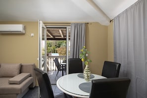 Ein Zimmer mit einer Couch, einem Esstisch mit Stühlen, einer Vase mit Blumen und einer Klimaanlage.