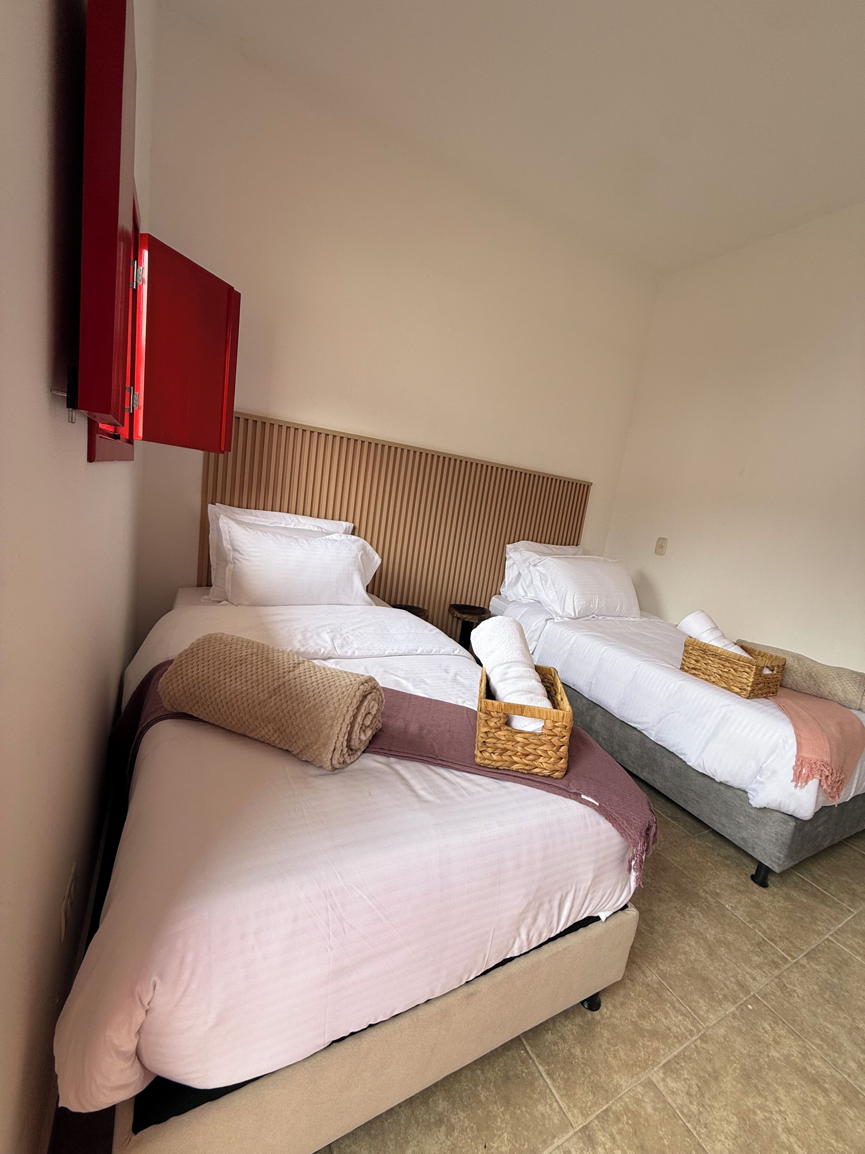 A hotel room with two beds, a wooden headboard, a red cabinet, and a small wooden stool.
