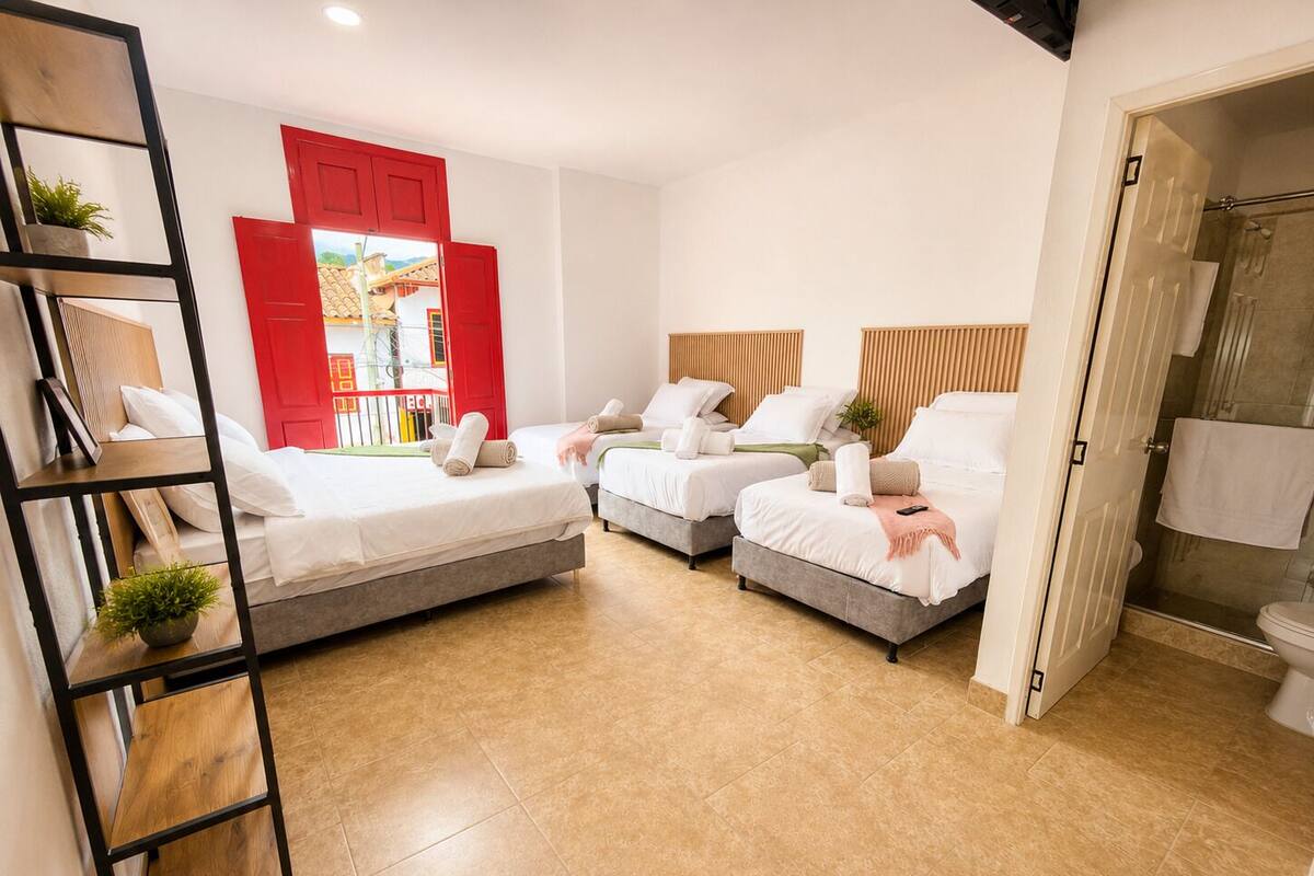 A hotel room with two beds, a red door, a shower, and a view of a building outside.