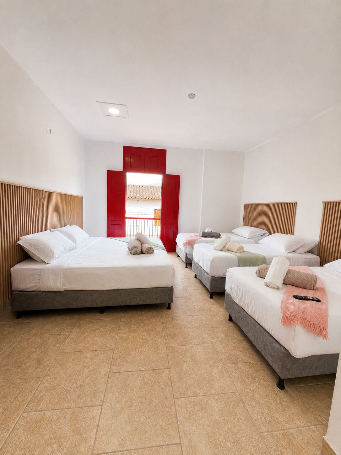 A hotel room with three beds, a red door, and a view of the outside.