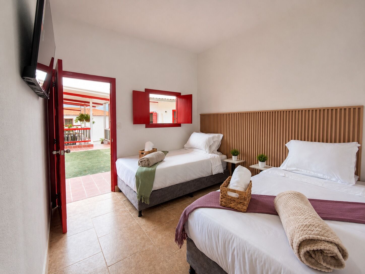 A hotel room with two beds, a TV, a small table, and a balcony.