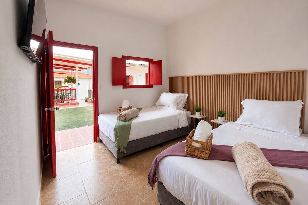A hotel room with two beds, a TV, a small table, and a balcony.