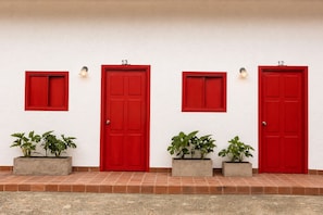 Four red doors with numbers 12, 13, and 14, each with a small window above and potted plants in front.