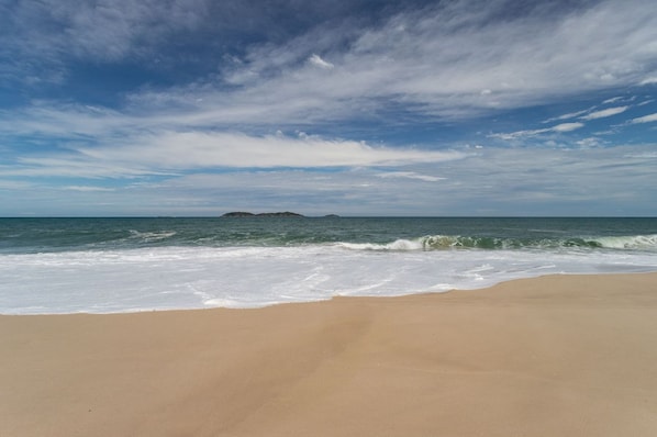 A beach with waves, a clear sky, and distant islands. - Casa com Churrasqueira a 550m da Praia Itaipua u (Marica)