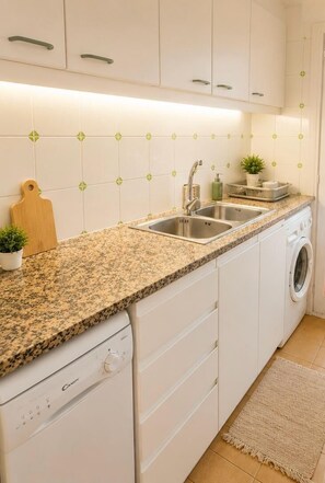 A compact kitchen with white cabinets, a granite countertop, a washing machine, and a tiled backsplash. - Sea View Apartment - Swimming pool and tennis (L'Escala)