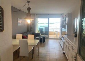 Een compacte leefruimte met een eethoek, een bank, een televisie en een balkon met uitzicht.