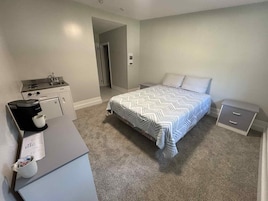 Un dormitorio con cama, mesita de noche, cómoda, cafetera y kitchenette.