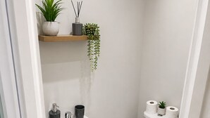 Un baño pequeño con un lavamanos, inodoro y una estantería con plantas y artículos de aseo.