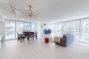 A spacious living area with large windows, a dining table, and a sofa. - Over 1000 SF Condo, free parking (Toronto)
