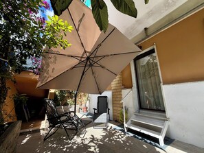 Eine Terrasse mit großem Sonnenschirm, einem Stuhl, einem kleinen Tisch und einer Tür, die auf einen Balkon führt.