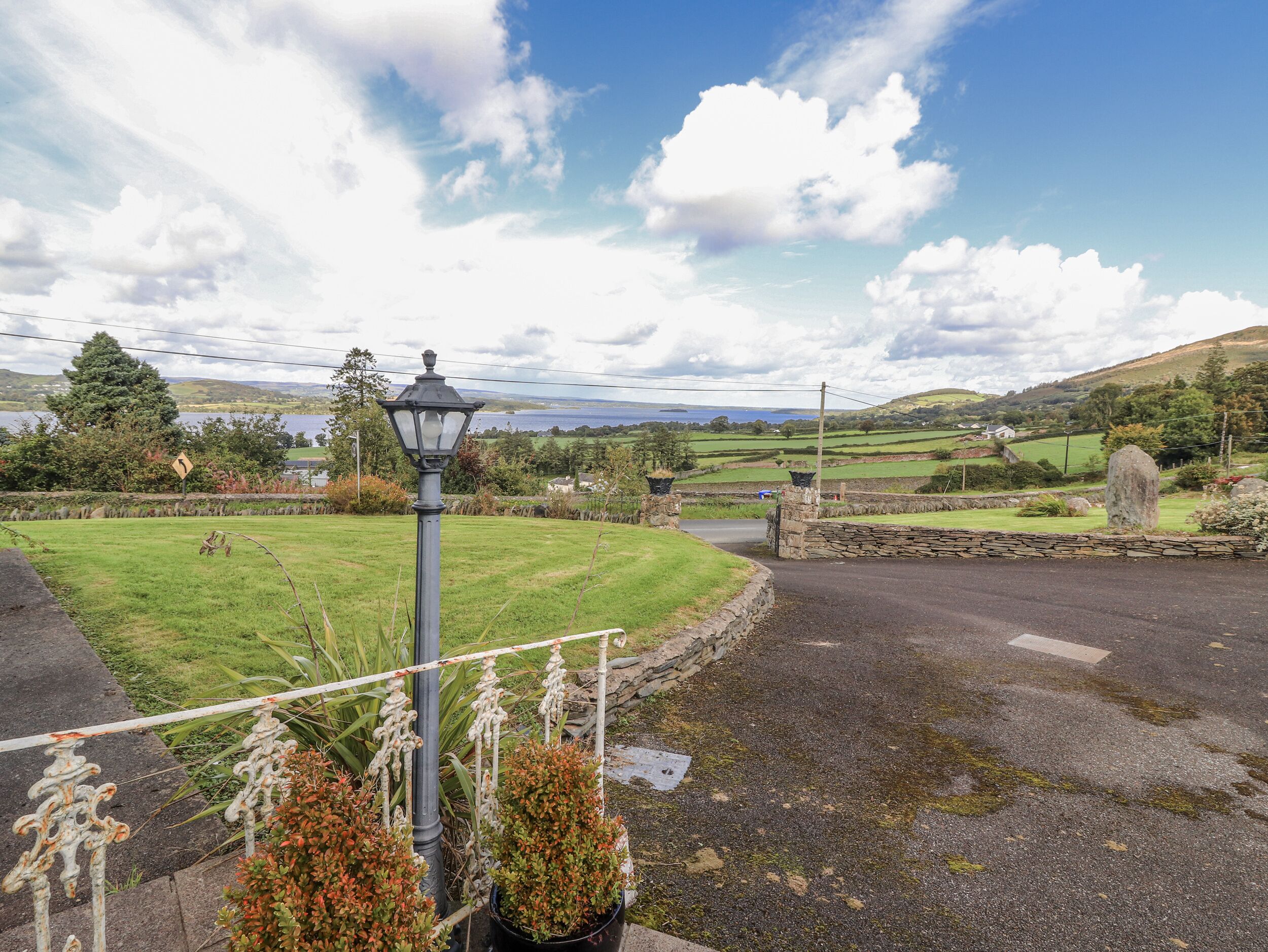 A rural landscape with a stone wall, a lamp post, and a grassy field.