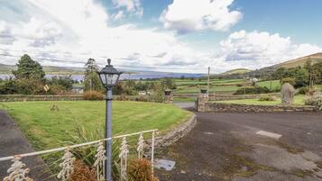 A rural landscape with a stone wall, a lamp post, and a grassy field.