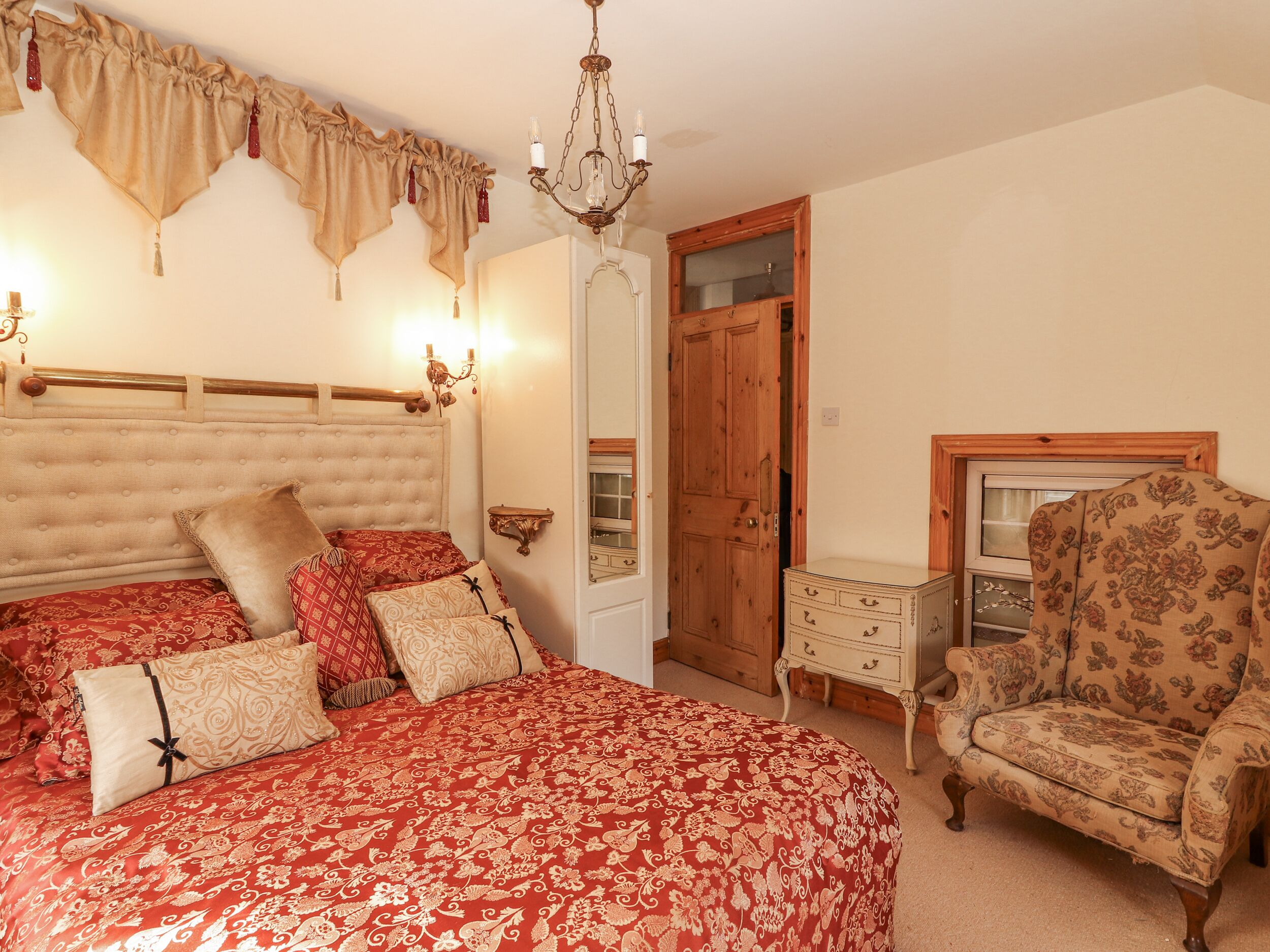 A bedroom with a large bed, a wooden wardrobe, a chair, and a chandelier.