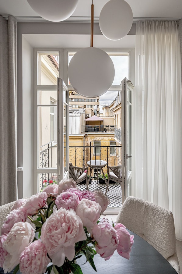 En balkon med udsigt til bygninger, et bord med stole og en blomstervase.