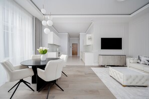Uma sala de estar moderna com área de refeições, televisão e cozinha ao fundo.
