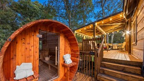 Una cabaña de madera con exterior circular, una terraza y una zona de estar al aire libre cubierta.