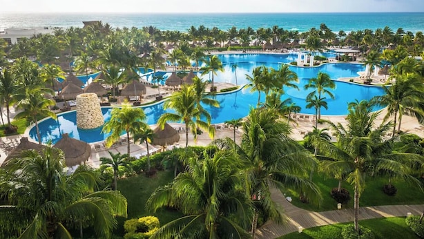 Ein Resort mit mehreren Swimmingpools, Palmen und Blick auf den Ozean.