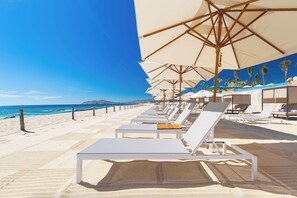 Ein Hotel direkt am Strand mit Liegestühlen, Sonnenschirmen und freiem Blick auf das Meer.