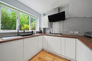 A kitchen with white cabinets, a wooden countertop, a window with a view of trees, and a built-in stove.