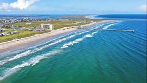 Eine Luftaufnahme einer Küstenregion mit Strand, Steg und einem großen Gebäude.