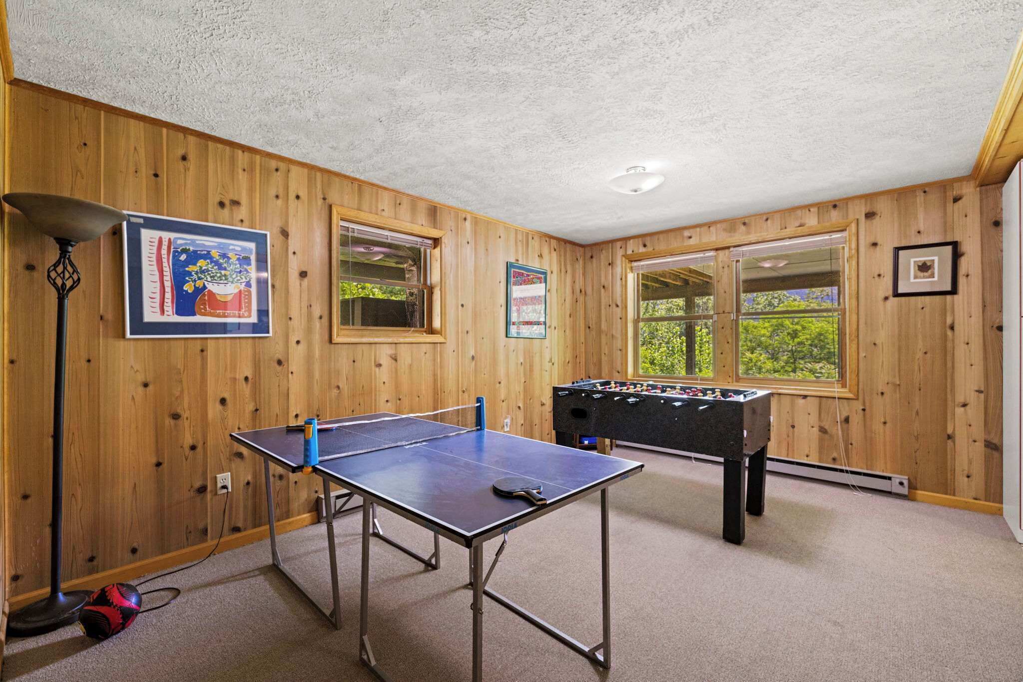 Una habitación con paredes de madera, mesa de ping pong, mesa de futbolín y ventanas amplias.