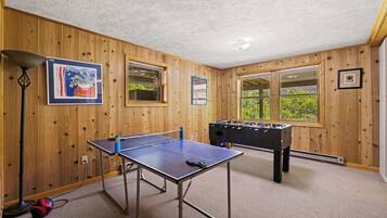 Una habitación con paredes de madera, mesa de ping pong, mesa de futbolín y ventanas amplias.