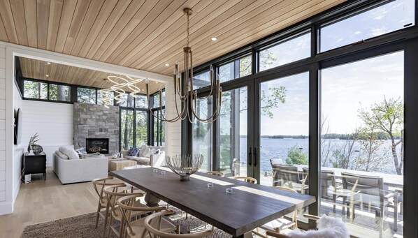Een modern interieur met een stenen open haard, een eethoek en grote ramen met uitzicht op een meer.