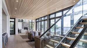 Een modern interieur met een stenen openhaard, houten plafond en grote ramen met uitzicht op de omgeving.