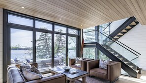 Un interior moderno con ventanas amplias, una escalera y un área de estar con vista al lago.