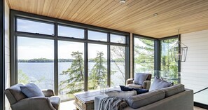 Un interior moderno con ventanas amplias, techo de madera y vista a un lago.